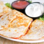 Cheesy quesadilla triangles served with dipping sauce on a white plate